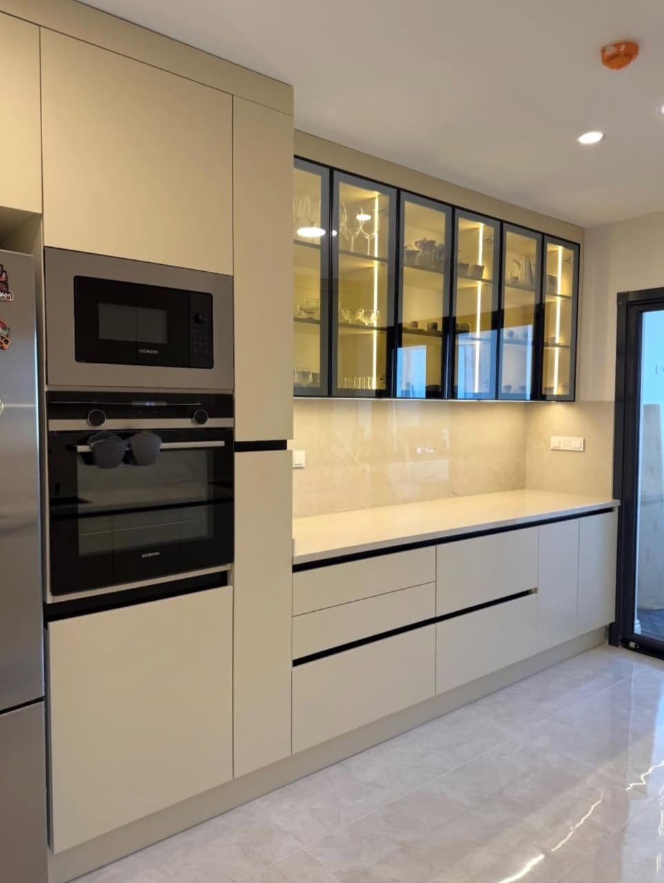 Warm cream cabinetry, tall glass display cabinets with internal lighting, and built-in appliances. Open, elegant, and ultra-functional. 🏆